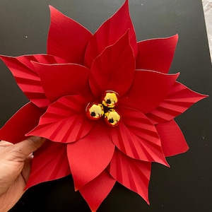 May include: A red paper poinsettia flower with three gold ornaments in the center.