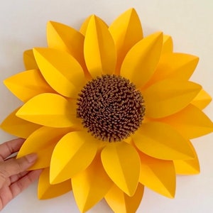 May include: A large paper sunflower with yellow petals and a brown center. The sunflower is made of paper and has a realistic appearance.