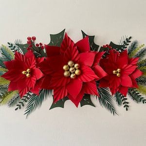 May include: A paper craft Christmas wreath with three red poinsettia flowers, green holly leaves, and gold ornaments.