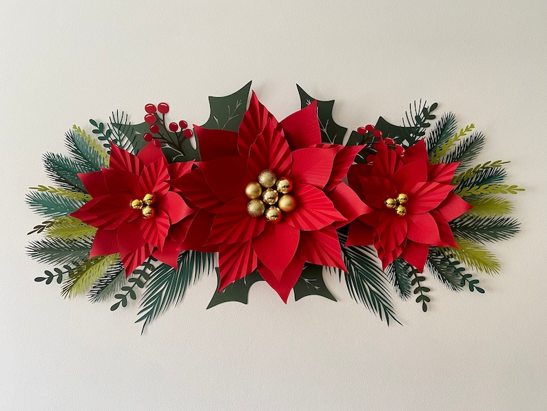 May include: A paper craft Christmas wreath with three red poinsettia flowers, green holly leaves, and gold ornaments.