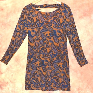 May include: A long-sleeved dress featuring a paisley pattern in shades of brown, blue, and purple. The dress has a scoop neckline and a fitted silhouette. The fabric appears to be a lightweight knit, suitable for various occasions.