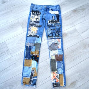 May include: Blue denim jeans featuring a patchwork design with various fabric squares in shades of brown, gray, white, and black. The patches include floral, geometric, and solid patterns, with visible frayed edges and stitching throughout the legs.