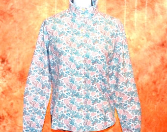 Puede incluir: Una camisa de manga larga con botones, cuello alto y un estampado floral repetitivo en tonos rosa suave, verde salvia y crema. La prenda presenta una hilera vertical central de botones pequeños y un corte estructurado con mangas largas.