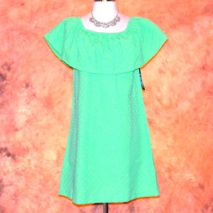 May include: A bright neon green dress featuring a wide, ruffled off-the-shoulder neckline and a subtle, repeating geometric textured pattern throughout the fabric. The garment has a straight, shift-style silhouette that falls to a mid-thigh length.