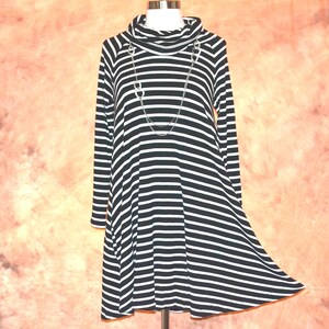 Könnte beinhalten: Ein langärmeliges Kleid mit schwarz-weißem Querstreifenmuster, Wasserfallausschnitt und ausgestellter Silhouette. Eine silberfarbene Gliederkette mit ovalen Elementen liegt um den Hals des Kleides und ruht auf dem Brustbereich.