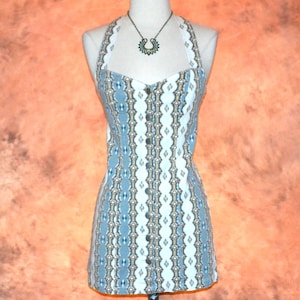 May include: A blue and white patterned halter dress with a button-down front. The dress features a geometric design and a white lace trim along the neckline. A silver-toned necklace with a pendant is also visible.