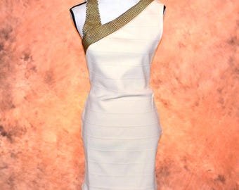 May include: A sleeveless cream-colored mini dress featuring a horizontal banded construction and a prominent gold-toned chainmail accent draped across the right shoulder and neckline, creating a structured, form-fitting silhouette on a mannequin.