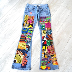 May include: Light blue denim jeans featuring a flared leg silhouette. The front panels of both legs are decorated with a patchwork design consisting of various colorful geometric and floral fabric patterns in shades of yellow, orange, pink, green, and blue.