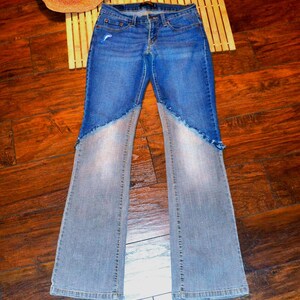 Könnte beinhalten: Blaue Jeans aus Denim mit einem einzigartigen Design. Die Jeans haben ein zweifarbiges Farbschema, mit einem helleren Denim-Ton an den Unterschenkeln und einem dunkleren Blau am oberen Teil. Die Jeans haben eine ausgestellte Beinöffnung.