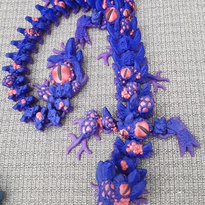 May include: A purple and pink segmented dragon figurine with multiple eyes. The dragon is curled into a circle shape.