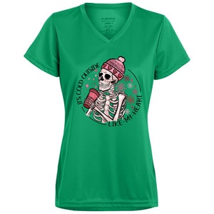 May include: Green V-neck t-shirt with a graphic of a skeleton wearing a pink beanie and holding a coffee cup. The graphic includes the text "It's cold outside like my heart" in a circular design with snowflakes.
