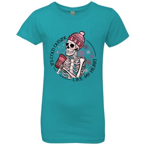 May include: Teal t-shirt featuring a skeleton graphic wearing a pink beanie with hearts and holding a red cup. The graphic includes the text "IT'S COLD OUTSIDE LIKE MY HEART" in a circular design with snowflakes.