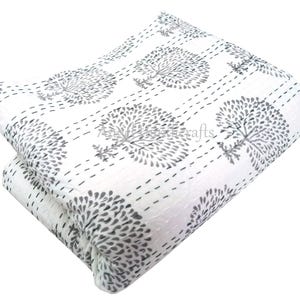 Könnte beinhalten: Gefaltete weiße Steppdecke mit einem sich wiederholenden Muster aus grauen Baummotiven. Die Bäume sind mit einem Punktlinienmuster handgenäht. Das Design der Steppdecke ist sichtbar und zeigt die Textur und die detaillierten Nähte. Die Ästhetik ist schlicht und elegant.
