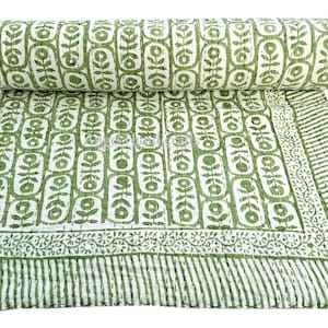 May include: A green and white patterned quilt with a floral design. The quilt is rolled up at the top, displaying the pattern. The quilt is made of a soft material and is suitable for a bed or sofa.