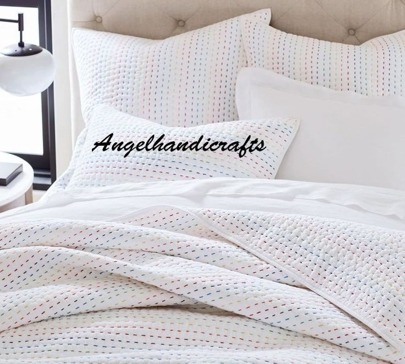 May include: White cotton quilt with colorful stitching in a random pattern. The quilt is on a bed with white pillowcases and a white pillow with the text "Angelhandicrafts" in black.
