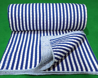 May include: A folded quilt featuring a pattern of bold royal blue and white vertical stripes. The fabric displays visible running stitch details throughout the surface, with a partially unfolded corner revealing a matching striped underside.