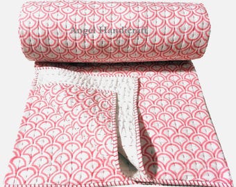 May include: A folded quilt featuring a repeating pink and white fan-shaped pattern with visible stitching throughout. The text Angel Handicraft is printed in gray across the center of the rolled portion of the fabric.