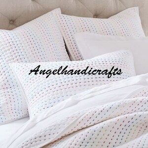 May include: White quilted pillowcases with a subtle colorful pattern. The pillowcases are arranged on a bed with a white duvet cover.