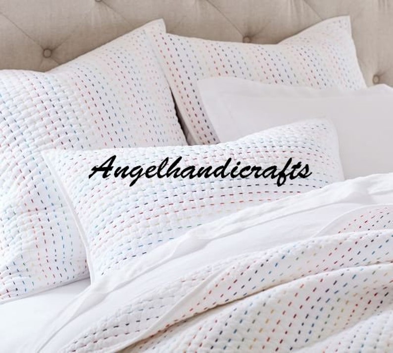May include: White quilted pillowcases with a subtle colorful pattern. The pillowcases are arranged on a bed with a white duvet cover.