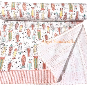 Op de afbeelding: Een witte katoenen quilt met een herhalend patroon van kleurrijke vissen in tinten oranje, geel en groenblauw. De stof heeft zichtbare stikseldetails en een gestreepte oranje rand. De tekst Angel Handicrafts is op de stof gedrukt.