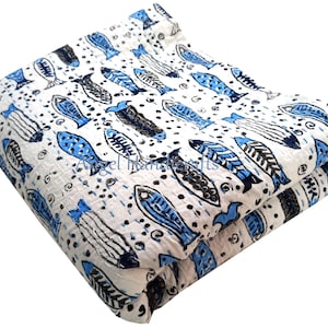 Peut inclure: Couverture blanche pliée avec un motif répétitif de poissons bleus et noirs. Les poissons sont stylisés avec différents motifs et sont répartis sur la surface. La couverture est faite d'un matériau doux et a une texture cousue.