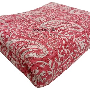 Op de afbeelding: Gevouwen roze en witte quilt met paisley-patroon. De quilt heeft een herhalend ontwerp van grote paisley-vormen en bloemelementen. De stof is effen roze van kleur met witte accenten. De tekst "Angel Handicrafts" is zichtbaar.