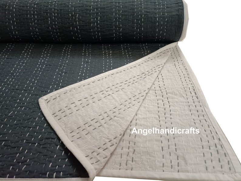 May include: A dark gray kantha quilt with white stitching. The quilt is folded in half, revealing a white underside with the same stitching pattern. The text "Angelhandicrafts" is visible on the white side.