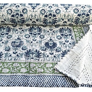 Puede incluir: Un edredón enrollado e impreso con un estampado floral en azul marino y blanco. El edredón está parcialmente desplegado, revelando un borde verde y blanco con un borde a rayas azul marino. El reverso es blanco.