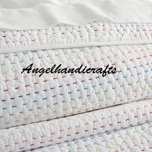 May include: White quilted throw blanket with colorful stitching. The blanket is folded in thirds and has a subtle texture.