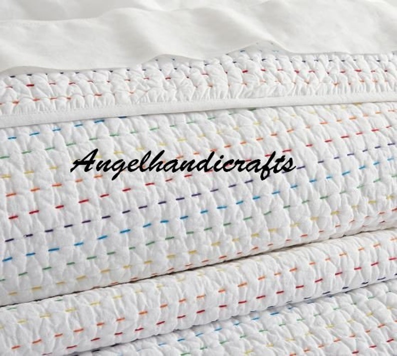May include: White quilted throw blanket with colorful stitching. The blanket is folded in thirds and has a subtle texture.