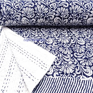 Könnte beinhalten: Eine aufgerollte Steppdecke mit einem marineblauen und weißen Blumenmuster. Das Design der Steppdecke ist ein sich wiederholendes weißes Blumenmotiv auf marineblauem Hintergrund. Die Rückseite ist weiß mit marineblauen Nähten. Der untere Rand hat marineblaue und weiße Streifen.