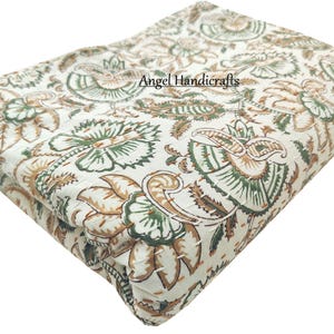 Op de afbeelding: Gevouwen witte quilt met een bloemenpatroon in groen- en bruintinten. De quilt heeft een herhalend ontwerp van gestileerde bloemen en bladeren. De tekst "Angel Handicrafts" is zichtbaar op de quilt.