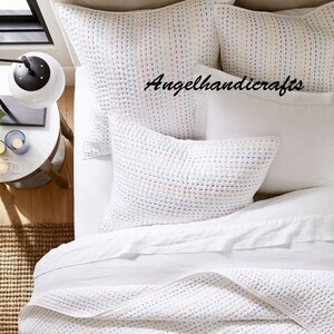 May include: White quilted bedding set with a white, quilted throw pillow and two white, quilted standard pillows. The pillows have a subtle, multi-colored pattern. The text "Angelhandicrafts" is visible on the bedding.