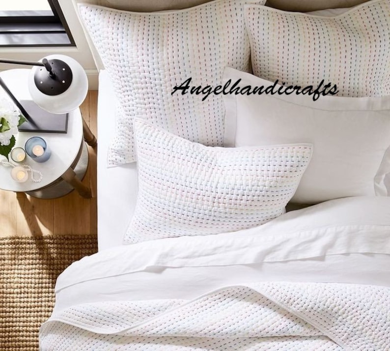 May include: White quilted bedding set with a white, quilted throw pillow and two white, quilted standard pillows. The pillows have a subtle, multi-colored pattern. The text "Angelhandicrafts" is visible on the bedding.