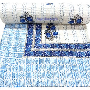 Könnte beinhalten: Eine weiß-blaue Steppdecke mit floralem Design. Die Steppdecke weist ein sich wiederholendes Muster aus blauen Blumen und Blättern auf weißem Hintergrund auf. Der Rand hat ein detailliertes blaues Blumenmuster. Die Steppdecke ist gefaltet und gerollt.