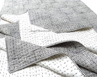 May include: A white and black reversible quilt with a striped pattern on one side and a dotted pattern on the other side. The quilt is made of cotton and is hand-stitched. The quilt is folded in half and the striped side is facing up. The quilt is made by Angel Handicraft.