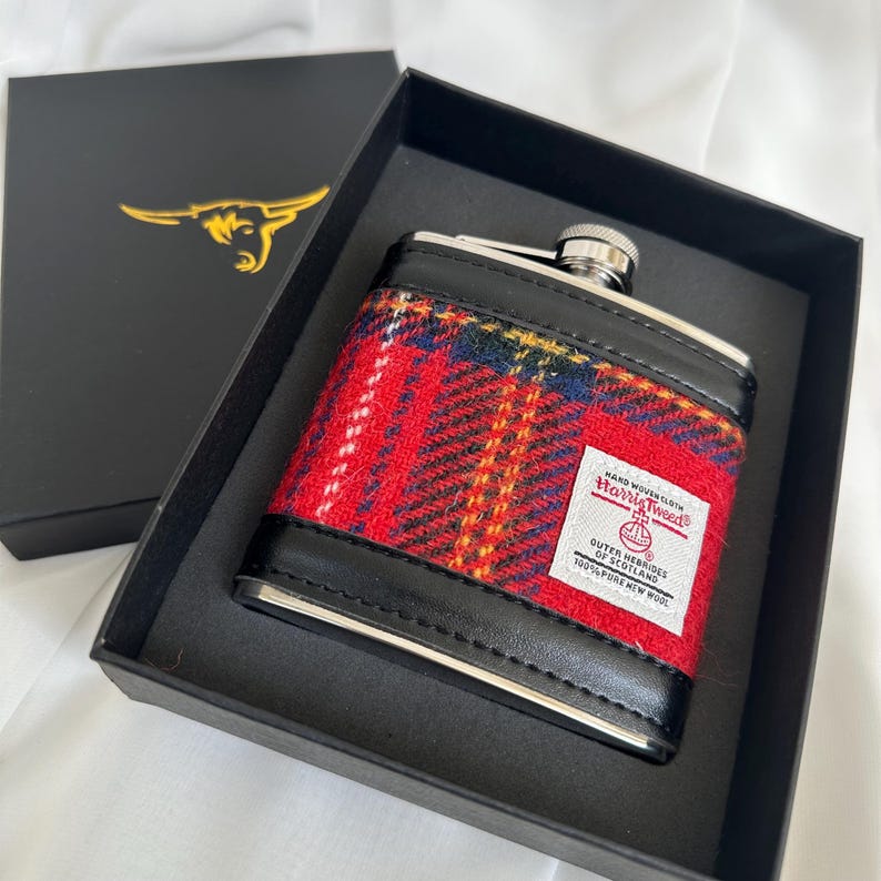 May include: A black box with a red and black flask inside. The flask is covered in a red, black, and yellow plaid fabric with a label that reads "Harris Tweed, Hand Woven Cloth, Outer Hebrides of Scotland, 100% Pure New Wool."