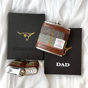 May include: Two brown gift boxes with gold lettering. The box on the left says "KERRENCE" and the box on the right says "DAD". A brown and green plaid hip flask with a silver top is sitting on top of the boxes.