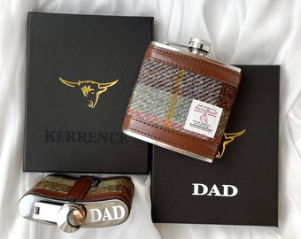 Pode incluir: Duas caixas de presente marrons com letras douradas. A caixa à esquerda diz "KERRENCE" e a caixa à direita diz "DAD". Uma garrafa de bolso de tecido xadrez marrom e verde com uma tampa prateada está em cima das caixas.