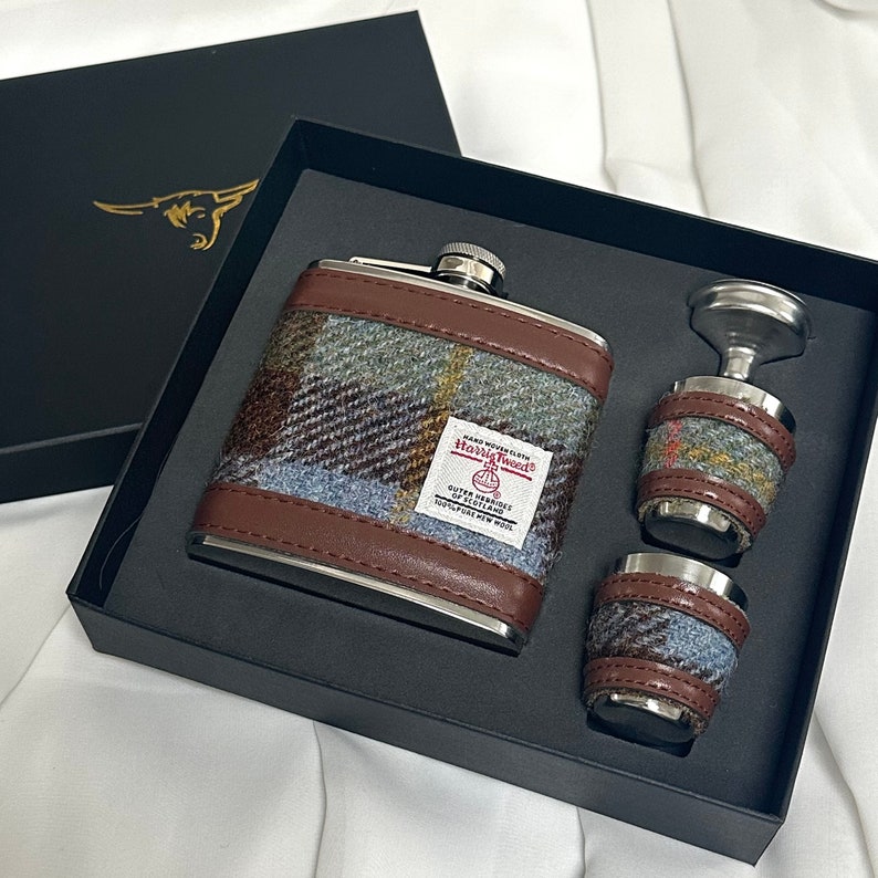 Pode incluir: Um conjunto de tr&ecirc;s frascos de prata com um padr&atilde;o de tweed marrom e azul. Os frascos est&atilde;o em uma caixa preta com as palavras "Harris Tweed" impressas no frasco maior.