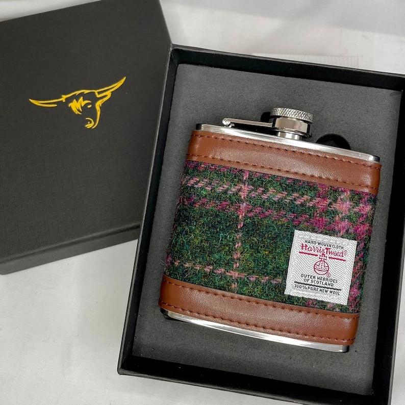 May include: A stainless steel hip flask with a brown leather trim and a green and pink plaid pattern. The flask has a label that reads "Hand Woven Cloth Harris Tweed Outer Hebrides of Scotland 100% Pure New Wool".