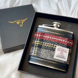 May include: A silver flask with a black leather cover and a red, green, and gray plaid pattern. The flask has a label that reads "Hand Woven Cloth Harris Tweed Outer Hebrides of Scotland 100% Pure New Wool".
