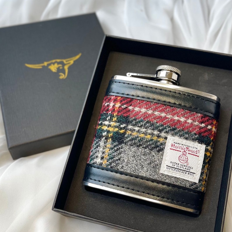 May include: A silver flask with a black leather cover and a red, green, and gray plaid pattern. The flask has a label that reads "Hand Woven Cloth Harris Tweed Outer Hebrides of Scotland 100% Pure New Wool".