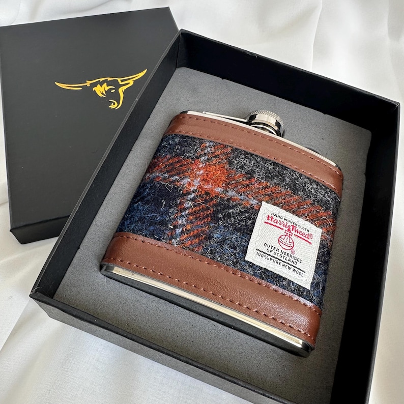 May include: A brown leather-covered flask with a silver top and a Harris Tweed label. The label reads "Harris Tweed Outer Hebrides Scotland 100% Pure New Wool".
