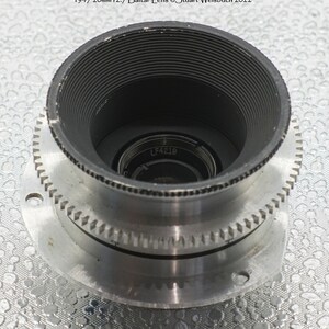 Puede incluir: Un objetivo de c&aacute;mara plateado con interior negro y un anillo de engranaje. El objetivo tiene el texto "LF4219" impreso en &eacute;l.