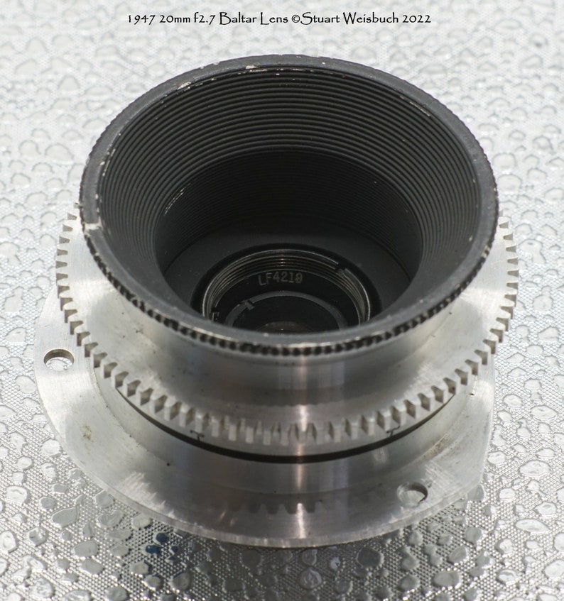 Puede incluir: Un objetivo de c&aacute;mara plateado con interior negro y un anillo de engranaje. El objetivo tiene el texto "LF4219" impreso en &eacute;l.