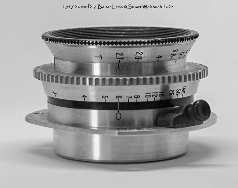 Puede incluir: Un objetivo de c&aacute;mara plateado con un anillo de apertura negro y una escala de profundidad de campo. El objetivo est&aacute; marcado con "1947 20mm f2.7 Baltar Lens Stuart Weisbuch 2022".