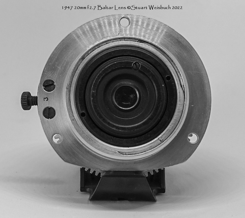 Puede incluir: Un objetivo de c&aacute;mara negro y plateado con una apertura de 20 mm f2.7. El objetivo est&aacute; etiquetado como "1947 20mm f2.7 Baltlar Lens &copy;Stuart Weisbuch 2022".