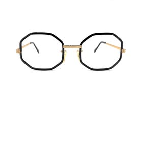 May include: Black octagonal eyeglasses with gold-colored accents. The frames have a geometric shape and a classic design. The lenses are clear, and the glasses are set against a white background.