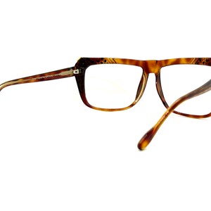 May include: Brown tortoise shell eyeglasses with gold accents. The glasses have a rectangular frame with a slight cat-eye shape.